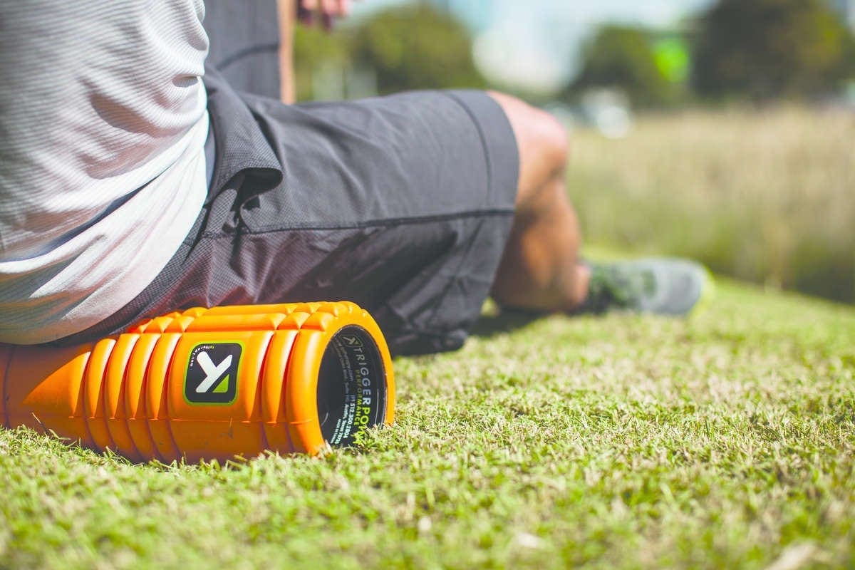 Person using orange foam roller on grass