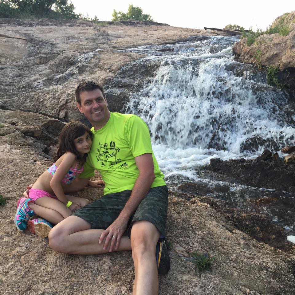 Smiling man and girl beside rocky waterfall