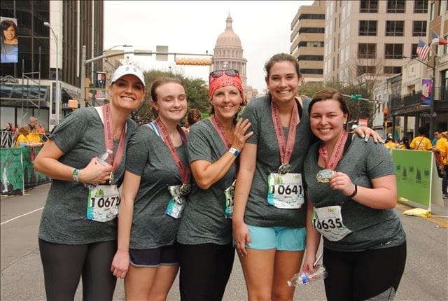 Five smiling runners with medals, state capitol