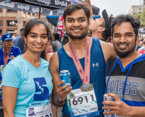 Three smiling marathon runners holding drinks and medal