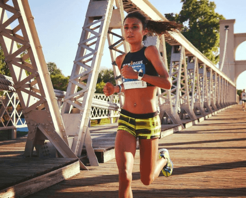 Young woman running across sunlit metal bridge