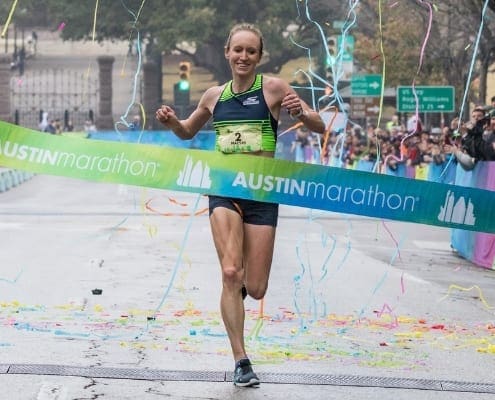 Female runner crossing Austin Marathon finish line