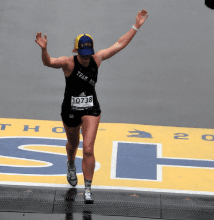 Runner crossing marathon finish line with arms raised