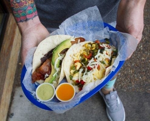 Image of male holding two Tacodeli tacos in a blue basket. Tacodeli is now the Official Taco of the Austin Marathon. Image of male holding two Tacodeli tacos in a blue basket. Tacodeli is now the Official Taco of the Austin Marathon.