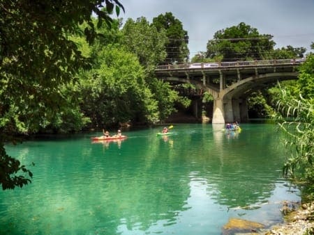 Kayakers paddling on turquoise river under bridge