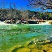 People on rocky riverbank near small waterfall