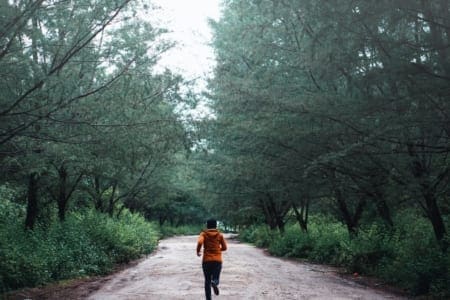 Person jogging on forest trail with orange jacket