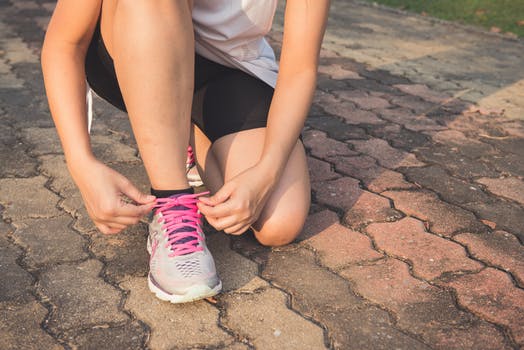 Person tying pink-laced running shoe on pavement