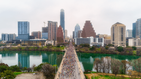 Crowd crossing bridge over river toward downtown skyline