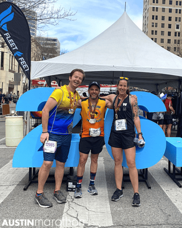 Three runners smiling by blue Austin Marathon sign