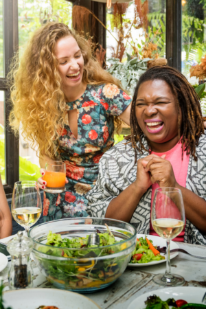 Two women laughing over salad and wine