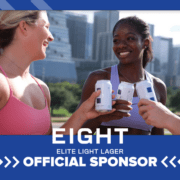 Three women clinking light lager cans outdoors