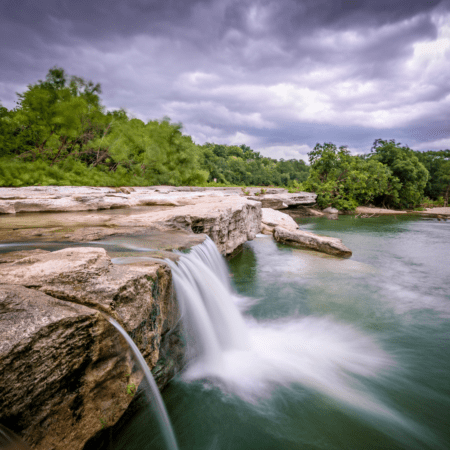 Waterfall over rocky ledge amid green trees Waterfall over rocky ledge amid green trees