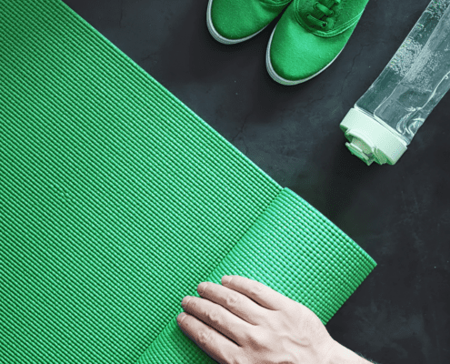 Hand rolling green yoga mat with sneakers