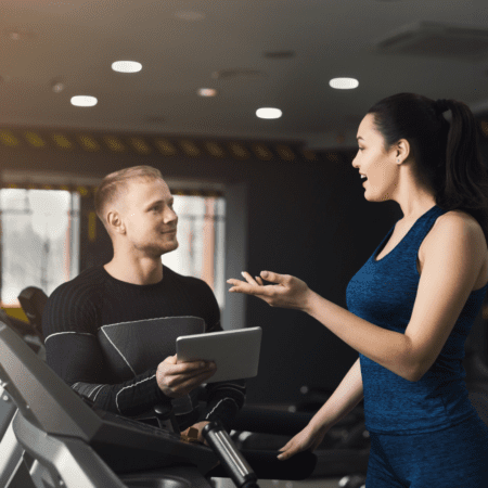 Female trainer instructing man on treadmill with tablet