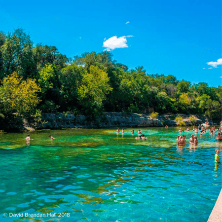Swimmers in clear turquoise river by trees
