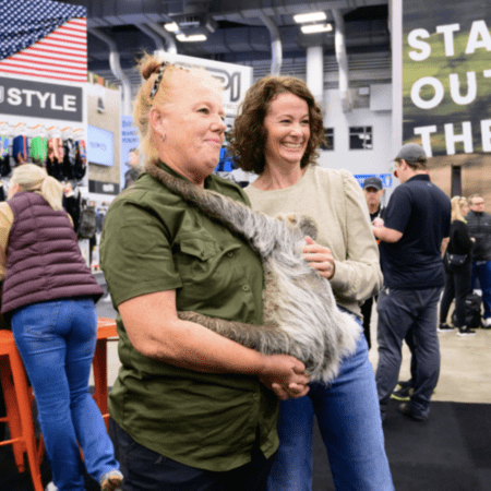 Two women smiling while holding a sloth