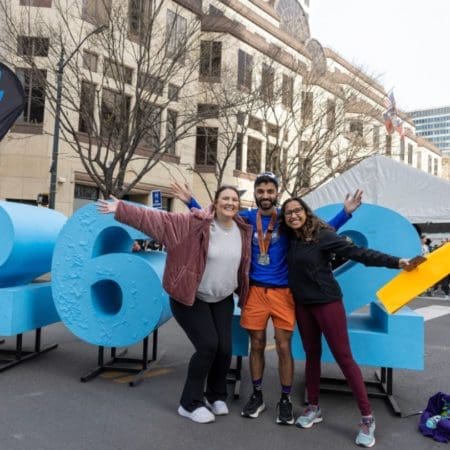 Three smiling runners posing by oversized blue numbers Three smiling runners posing by oversized blue numbers