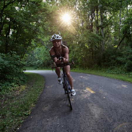 Cyclist riding road bike through sunlit woods