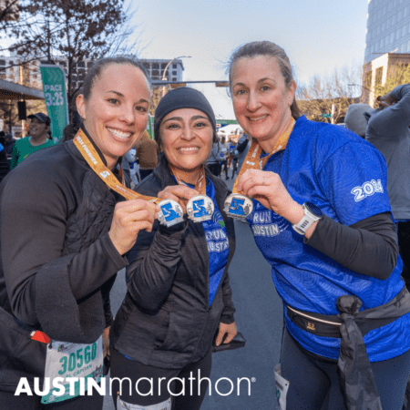 Three smiling marathon runners proudly display their medals after completing the Austin Marathon. Dressed in running attire, they stand together in a celebratory pose. A "PACE 3:25" sign and other participants are visible in the background, debunking common marathon myths. The text "Austin Marathon" is at the bottom. Austin Marathon Half Marathon & 5K Three smiling marathon runners proudly display their medals after completing the Austin Marathon. Dressed in running attire, they stand together in a celebratory pose. A "PACE 3:25" sign and other participants are visible in the background, debunking common marathon myths. The text "Austin Marathon" is at the bottom. Austin Marathon Half Marathon & 5K