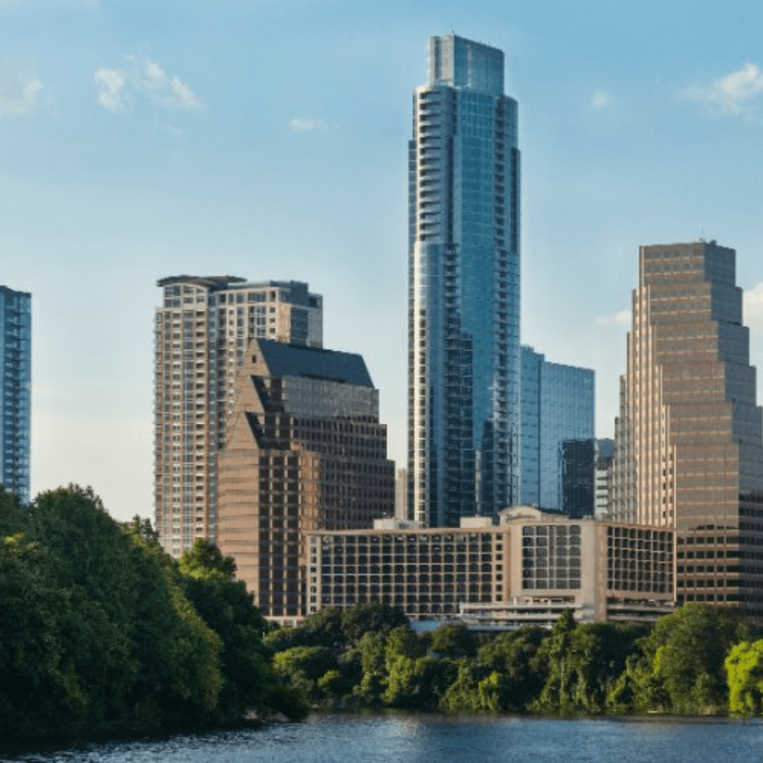 A city skyline featuring tall, modern skyscrapers alongside older buildings invites you to visit its charm. The scene includes a river in the foreground with lush green trees lining the water, set against a clear blue sky perfect for admiring from your hotel room. Austin Marathon Half Marathon & 5K A city skyline featuring tall, modern skyscrapers alongside older buildings invites you to visit its charm. The scene includes a river in the foreground with lush green trees lining the water, set against a clear blue sky perfect for admiring from your hotel room. Austin Marathon Half Marathon & 5K