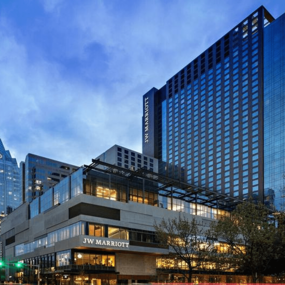 Evening view of the JW Marriott hotel, its modern architecture and glass facade gleaming under a vibrant blue sky. Trees line the street below, adding a touch of nature to this urban oasis. Inside, luxurious rooms await guests savoring the perfect race day or those exploring nearby hotels. Austin Marathon Half Marathon & 5K Evening view of the JW Marriott hotel, its modern architecture and glass facade gleaming under a vibrant blue sky. Trees line the street below, adding a touch of nature to this urban oasis. Inside, luxurious rooms await guests savoring the perfect race day or those exploring nearby hotels. Austin Marathon Half Marathon & 5K