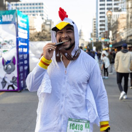 Smiling marathon runner in chicken costume biting medal Smiling marathon runner in chicken costume biting medal