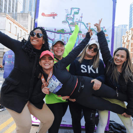 Five women, joyful runners, strike a playful pose in front of a colorful marathon map at the Marathon in Austin. One is lifted horizontally by her friends—all wear casual athletic clothing, hats, and sunglasses, looking happy and celebratory. Austin Marathon Half Marathon & 5K Five women, joyful runners, strike a playful pose in front of a colorful marathon map at the Marathon in Austin. One is lifted horizontally by her friends—all wear casual athletic clothing, hats, and sunglasses, looking happy and celebratory. Austin Marathon Half Marathon & 5K