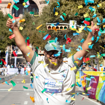 A smiling runner with a beard and glasses raises his arms in celebration as colorful confetti falls around him at the Marathon in Austin finish line. He wears a cap, sports shirt, and bib number 4402, embodying the spirit of all dedicated runners. Austin Marathon Half Marathon & 5K A smiling runner with a beard and glasses raises his arms in celebration as colorful confetti falls around him at the Marathon in Austin finish line. He wears a cap, sports shirt, and bib number 4402, embodying the spirit of all dedicated runners. Austin Marathon Half Marathon & 5K