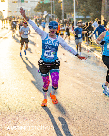 A smiling runner in colorful gear with "JENN" on her shirt spreads her arms wide during the Austin Marathon race, captured in vibrant Official Race Photos with other runners and spectators cheering along the sunlit street. Austin Marathon Half Marathon & 5K A smiling runner in colorful gear with "JENN" on her shirt spreads her arms wide during the Austin Marathon race, captured in vibrant Official Race Photos with other runners and spectators cheering along the sunlit street. Austin Marathon Half Marathon & 5K
