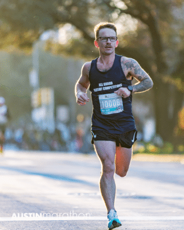 A male runner wearing a black tank top and glasses races in the Austin Marathon, race bib number 10006 visible. Sunlight and trees provide a scenic backdrop for this personal moment captured in official race photos. Austin Marathon Half Marathon & 5K A male runner wearing a black tank top and glasses races in the Austin Marathon, race bib number 10006 visible. Sunlight and trees provide a scenic backdrop for this personal moment captured in official race photos. Austin Marathon Half Marathon & 5K