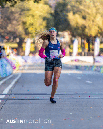 A female runner with a race bib and pink arm sleeves races down a city street during the Austin Marathon, with blurred trees and spectators in the background. The image captures an exciting personal moment from the Official Race Photos collection. Austin Marathon Half Marathon & 5K A female runner with a race bib and pink arm sleeves races down a city street during the Austin Marathon, with blurred trees and spectators in the background. The image captures an exciting personal moment from the Official Race Photos collection. Austin Marathon Half Marathon & 5K