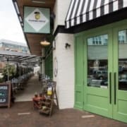 A restaurant with pale green double doors and a black-and-white striped awning, Flower Child is a favorite among healthy dining Austin spots. Outdoor seating lines the sidewalk under a matching awning, welcoming health-conscious diners. Austin Marathon Half Marathon & 5K