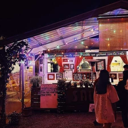 A cozy food stall in Austin, decorated with string lights and red curtains, is open at night. People gather outside, while colorful lights create a warm, inviting vibe—perfect for carb-loading restaurant lovers seeking late-night bites. Austin Marathon Half Marathon & 5K