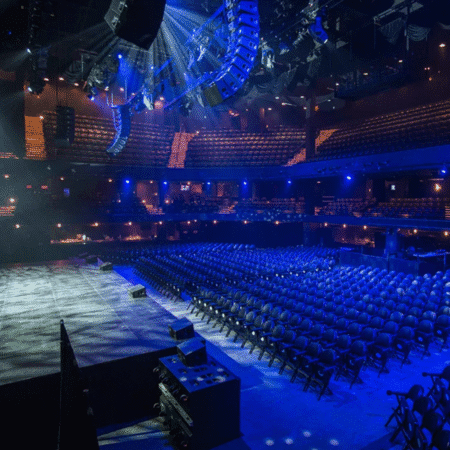 An empty concert hall with rows of seats facing a large stage, illuminated by blue and purple stage lights—one of the best spots in Austin where to watch live music. Upper balconies and sound equipment are visible in the spacious, modern venue. Austin Marathon Half Marathon & 5K