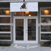Glass storefront of MYO Massage, Austin’s Massage & Bodywork Center. A white sign with the business name and contact info hangs above the entrance. A hidden gem in Austin, perfect for post-run recovery. The words “Austin-Grown” appear at the bottom. Austin Marathon Half Marathon & 5K