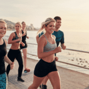 A group of young adults jogging together along a waterfront promenade on a sunny day, smiling as they overcome mental hurdles and enjoy staying motivated during their run with the sea and cityscape in the background. Austin Marathon Half Marathon & 5K
