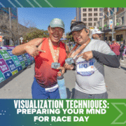 Two smiling runners in athletic gear hold medals and pose at the race finish line, surrounded by banners and city buildings. Text at the bottom reads: "Visualization Techniques: Preparing Your Mind for Race Day.”. Austin Marathon Half Marathon & 5K