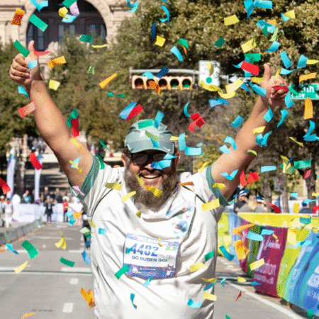 A smiling runner with a beard and glasses raises both thumbs up while colorful confetti falls around him at a race finish line, celebrating his achievement and motivation during training. Trees and spectators line the street in the background. Austin Marathon Half Marathon & 5K A smiling runner with a beard and glasses raises both thumbs up while colorful confetti falls around him at a race finish line, celebrating his achievement and motivation during training. Trees and spectators line the street in the background. Austin Marathon Half Marathon & 5K