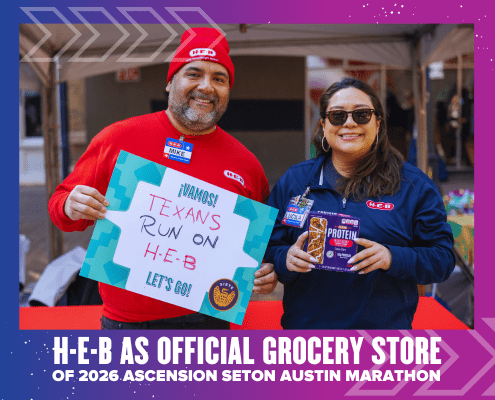 Two H-E-B employees smile at an event. The man holds a “¡VAMOS! Texans run on H-E-B” sign, while the woman displays protein bars. A banner announces H-E-B as the official grocery store of the Ascension Seton Austin Marathon. Austin Marathon Half Marathon & 5K