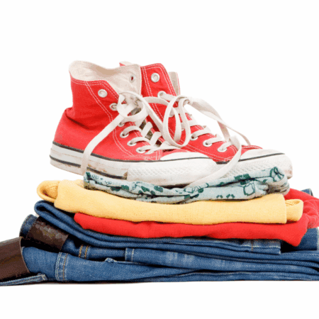 A pair of red high-top sneakers sits on top of a neatly folded stack of race day essentials—yellow shirt, red sweater, patterned fabric, and blue jeans—perfect for packing in your Austin Marathon gear bag, all set against a white background. Austin Marathon Half Marathon & 5K