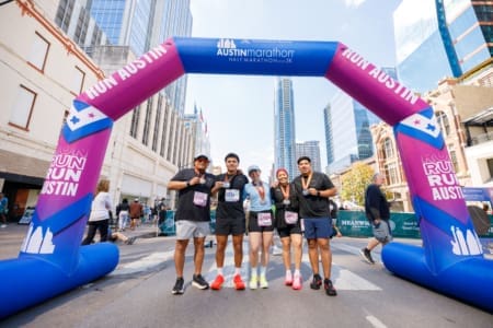 Five runners posing under Austin Marathon finish arch