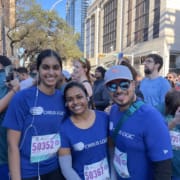 Three runners in blue shirts smiling at race
