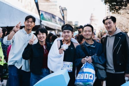 A group of five people, including a runner wearing a medal and race bib, smile and pose together at an outdoor fundraising event with tents and a crowd in the background. Austin Marathon Half Marathon & 5K A group of five people, including a runner wearing a medal and race bib, smile and pose together at an outdoor fundraising event with tents and a crowd in the background. Austin Marathon Half Marathon & 5K