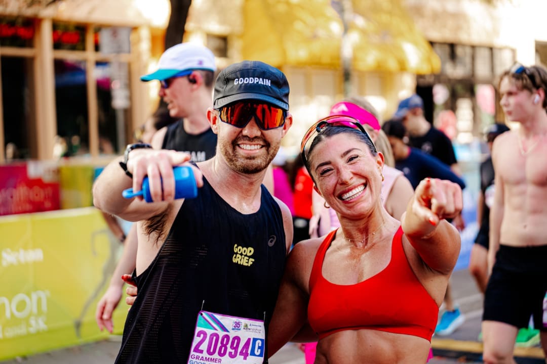 Two smiling runners, a man in a black tank top and cap and a woman in a red sports bra, point at the camera after finishing a race—perfect for Friends and Family Teams or team building group activities, with fellow participants and a colorful outdoor backdrop. Austin Marathon Half Marathon & 5K Two smiling runners, a man in a black tank top and cap and a woman in a red sports bra, point at the camera after finishing a race—perfect for Friends and Family Teams or team building group activities, with fellow participants and a colorful outdoor backdrop. Austin Marathon Half Marathon & 5K