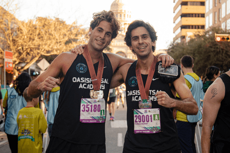 Two runners in “Oasis Futsal Academy” tank tops, proudly wearing medals and race bibs, smile after a race. Behind them, fellow participants and a domed building set the scene—echoing the camaraderie found in collegiate teams. Austin Marathon Half Marathon & 5K Two runners in “Oasis Futsal Academy” tank tops, proudly wearing medals and race bibs, smile after a race. Behind them, fellow participants and a domed building set the scene—echoing the camaraderie found in collegiate teams. Austin Marathon Half Marathon & 5K