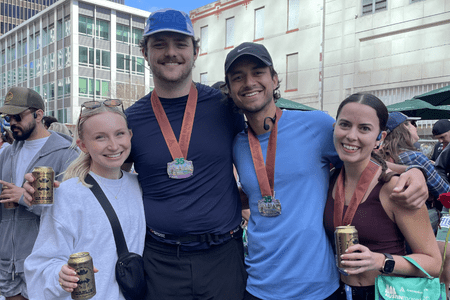 Four smiling people stand close together outdoors, proudly wearing running medals around their necks and holding cans, likely after completing a race with their social teams. Buildings and other participants are visible in the background, celebrating their training efforts. Austin Marathon Half Marathon & 5K Four smiling people stand close together outdoors, proudly wearing running medals around their necks and holding cans, likely after completing a race with their social teams. Buildings and other participants are visible in the background, celebrating their training efforts. Austin Marathon Half Marathon & 5K
