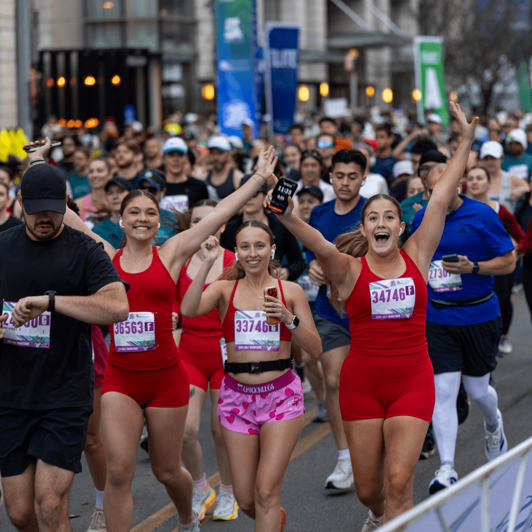 A group of runners, including three women in red outfits, smile and cheer with arms raised as they participate in the Ascension Seton Austin Marathon among a large crowd of competitors on a bustling city street. Austin Marathon Half Marathon & 5K A group of runners, including three women in red outfits, smile and cheer with arms raised as they participate in the Ascension Seton Austin Marathon among a large crowd of competitors on a bustling city street. Austin Marathon Half Marathon & 5K
