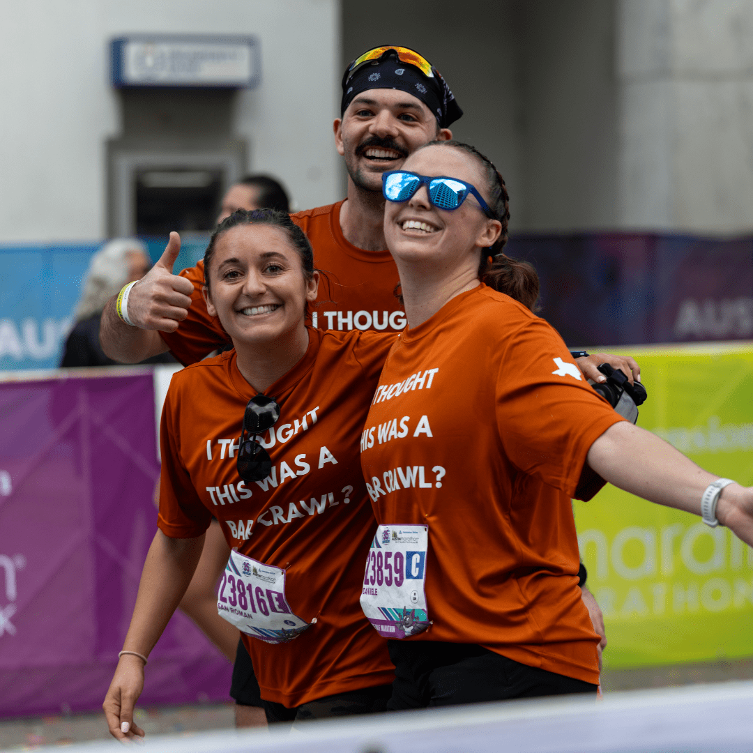 Three smiling runners in matching orange shirts pose at the Ascension Seton Austin Marathon finish line, two women in front and a man behind giving a thumbs-up. Their shirts humorously read, “I thought this was a bar crawl?!”. Austin Marathon Half Marathon & 5K Three smiling runners in matching orange shirts pose at the Ascension Seton Austin Marathon finish line, two women in front and a man behind giving a thumbs-up. Their shirts humorously read, “I thought this was a bar crawl?!”. Austin Marathon Half Marathon & 5K