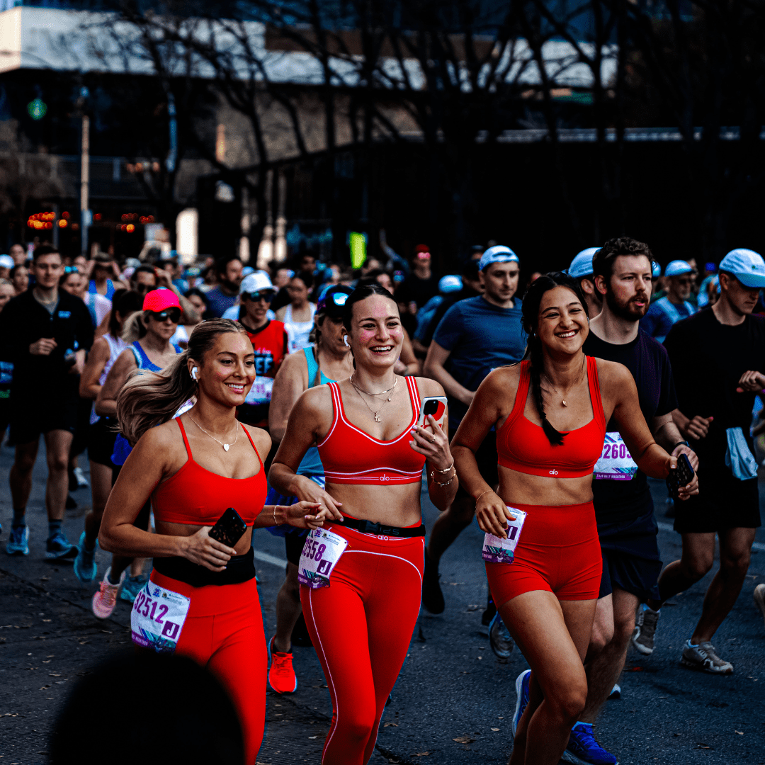 Three women in matching red athletic outfits run and smile together during the Ascension Seton Austin Marathon, surrounded by other racers. All wear bibs and seem to be enjoying the event, with trees and city buildings in the background. Austin Marathon Half Marathon & 5K Three women in matching red athletic outfits run and smile together during the Ascension Seton Austin Marathon, surrounded by other racers. All wear bibs and seem to be enjoying the event, with trees and city buildings in the background. Austin Marathon Half Marathon & 5K
